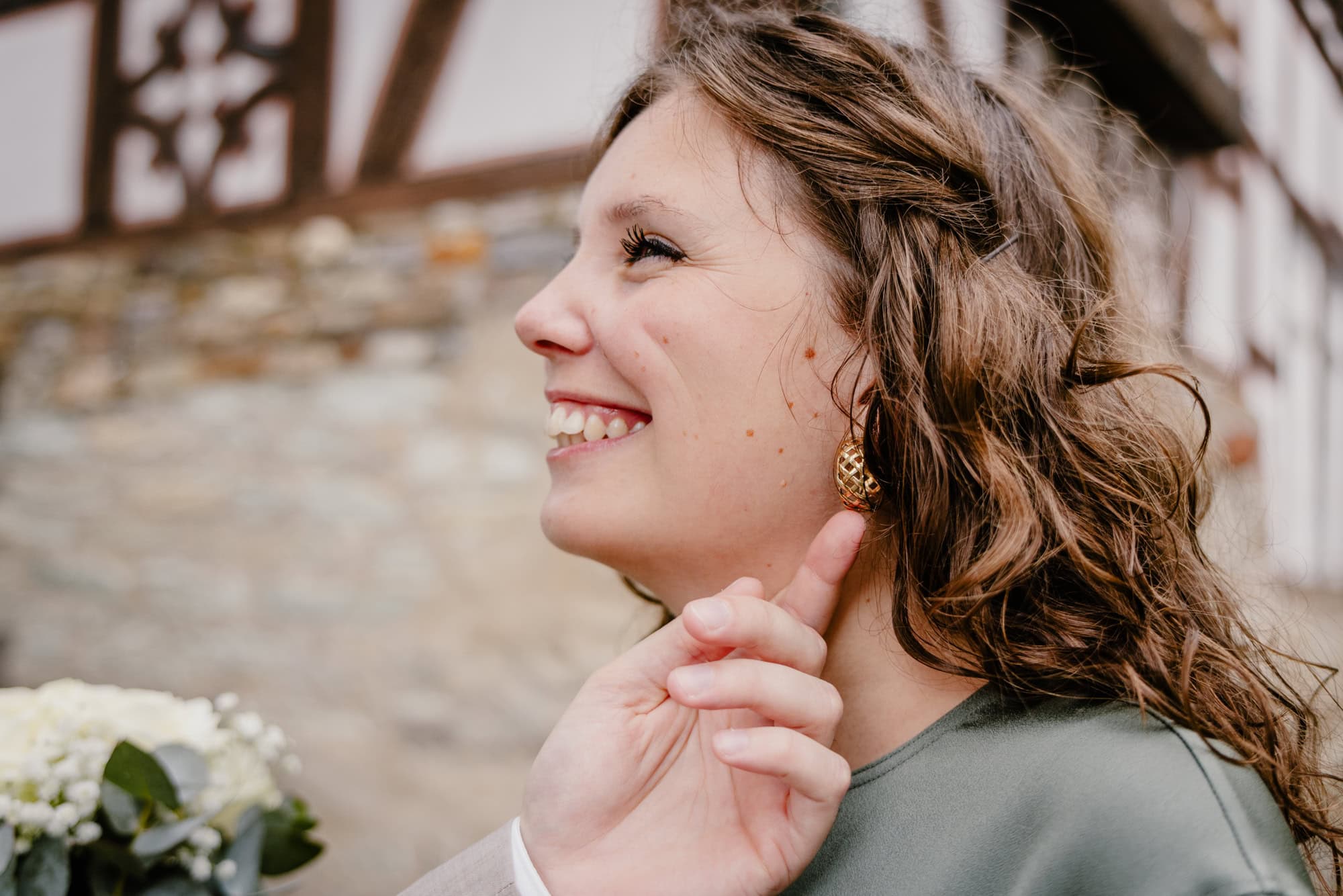 Ungestelltes Porträt – Braut lächelt während sich der Bräutigam ihren Ohrring anschaut