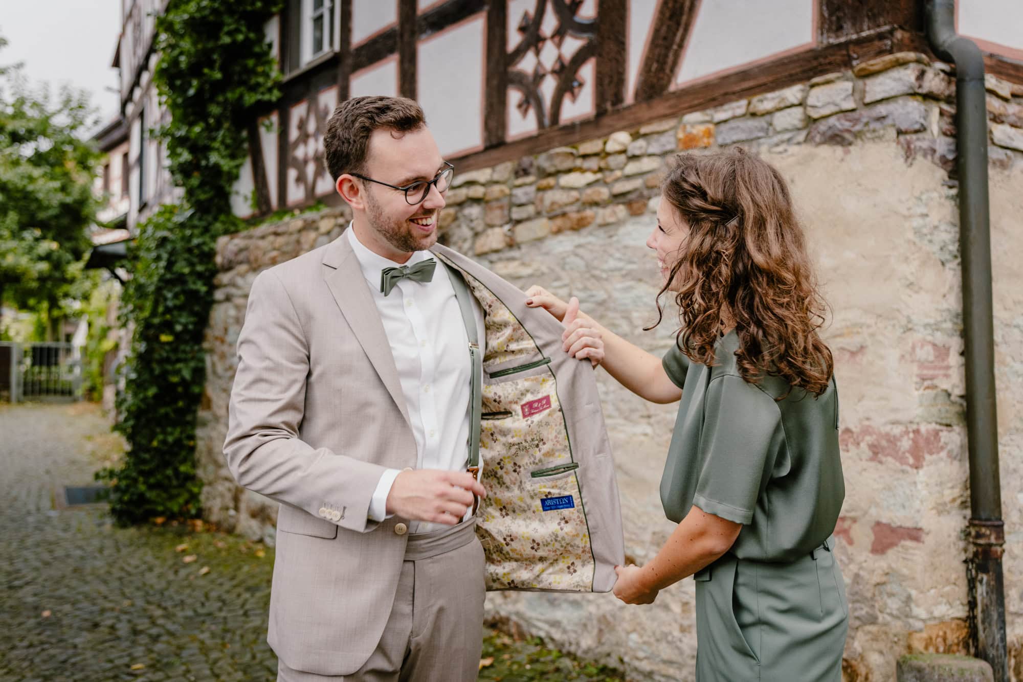 First Look Hochzeit in Oberursel – Bräutigam zeigt seiner Partnerin das Innenfutter seines Jackets